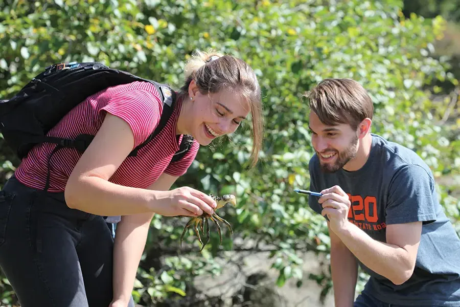 two students standing at a river inspecting a crawdad